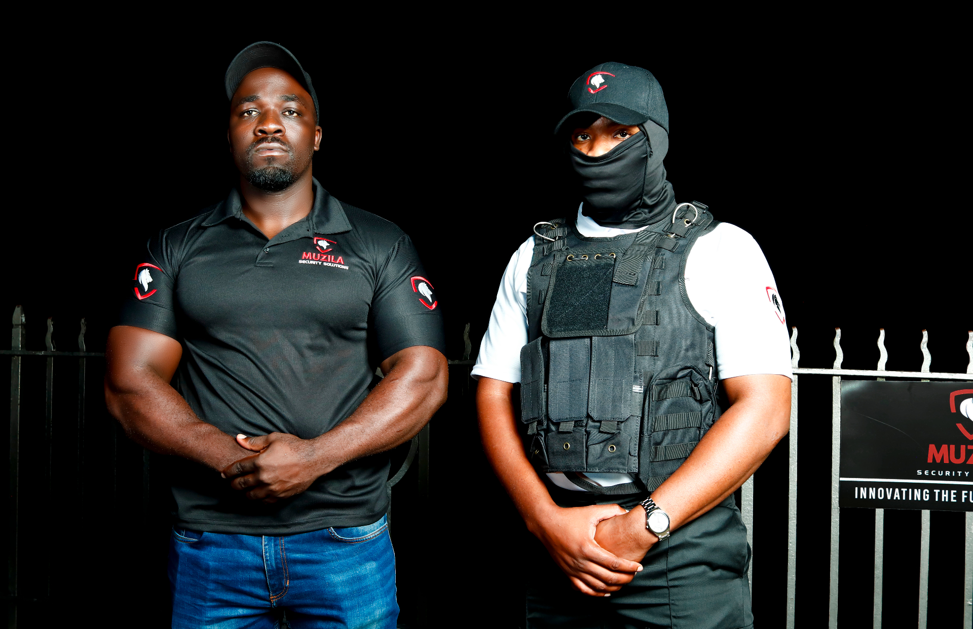 Two Muzila officers walking a residential estate perimeter, radios in hand, alert to the grounds around them.